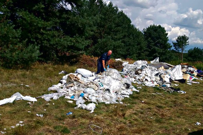 gora_plastikowcyh_smieci_i_policjant_ja_przeszukujacy Sterta odpadów pod lasem w Wał Rudzie