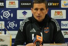 Trener Bruk-Bet Termaliki Nieciecza Marcin Brosz wypowiada się do mikrofonu na tle ścianki reklamowej podczas konferencji prasowej po meczu PKO BP Ekstraklasy